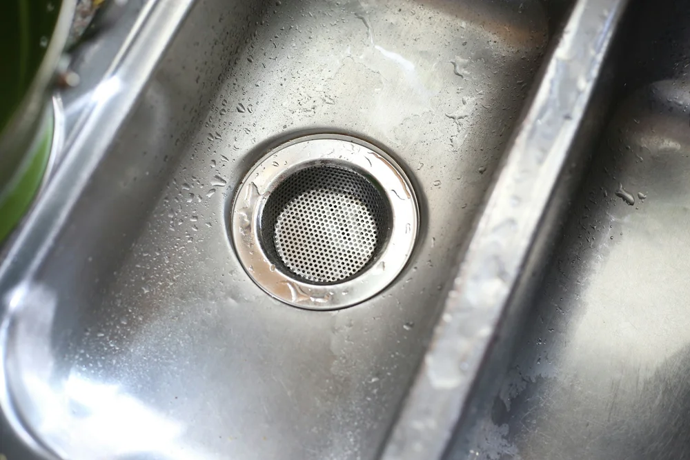 Empty stainless steel kitchen sink with water droplets and drain