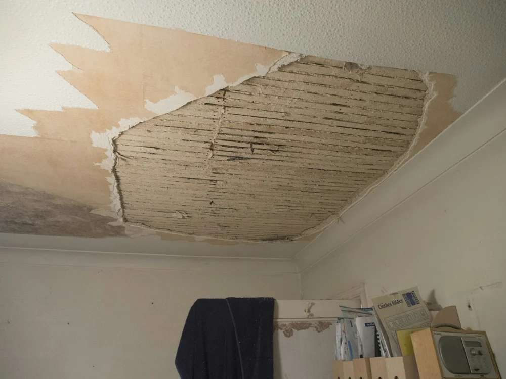 Ceiling with a large section of damaged plasterboard removed, exposing wooden beams underneath